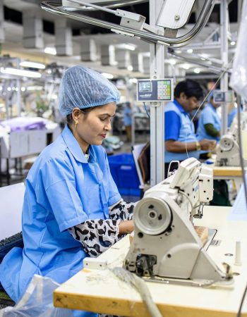 Os trabalhadores de uma fábrica têxtil, a operar máquinas de costura, vestidos com uniformes azuis e com redes no cabelo, estavam concentrados nas suas tarefas.